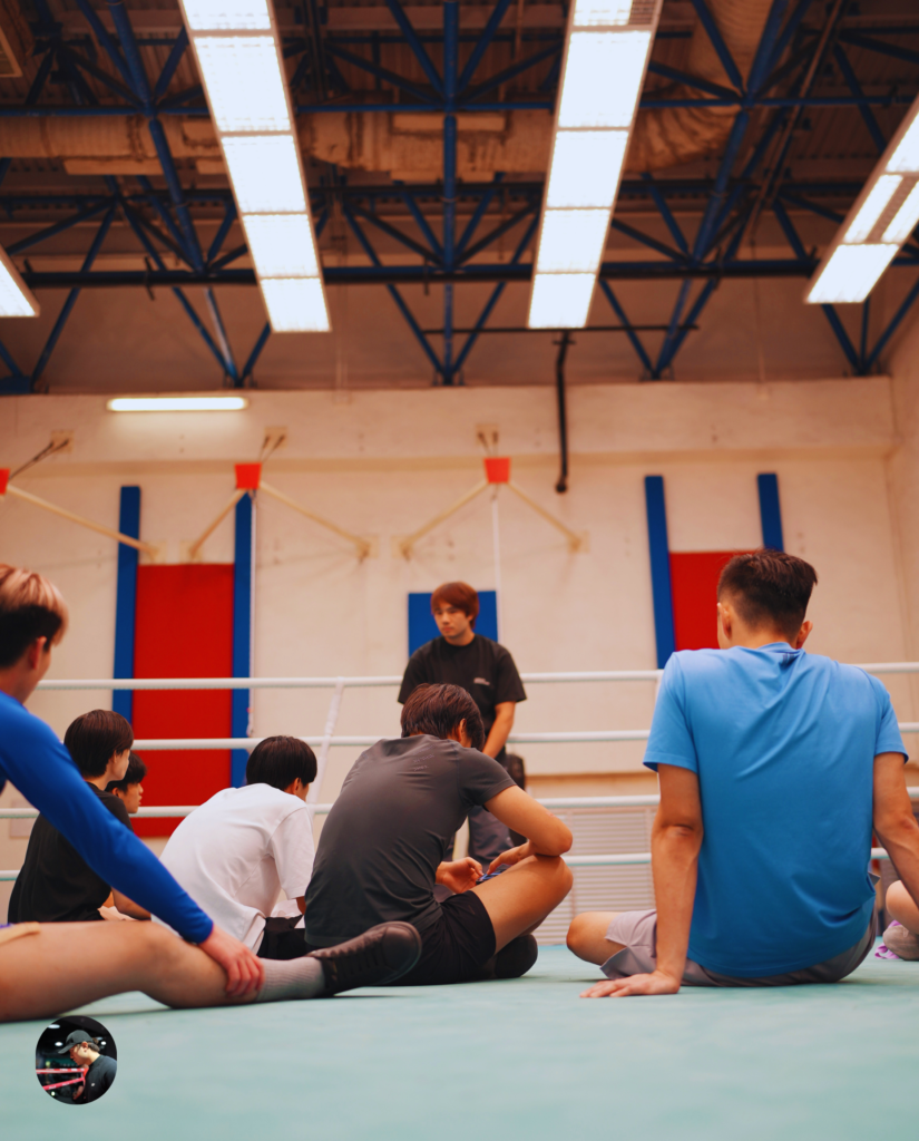 A boxing coach sits on the ring canvas instructing a group of attentive students. The summary text clarifies that professional boxing is not inherently "stronger" than amateur boxing, as many pro kings start as Olympians. A call-to-action banner encourages viewers to DM to book a trial class to learn Olympic boxing.